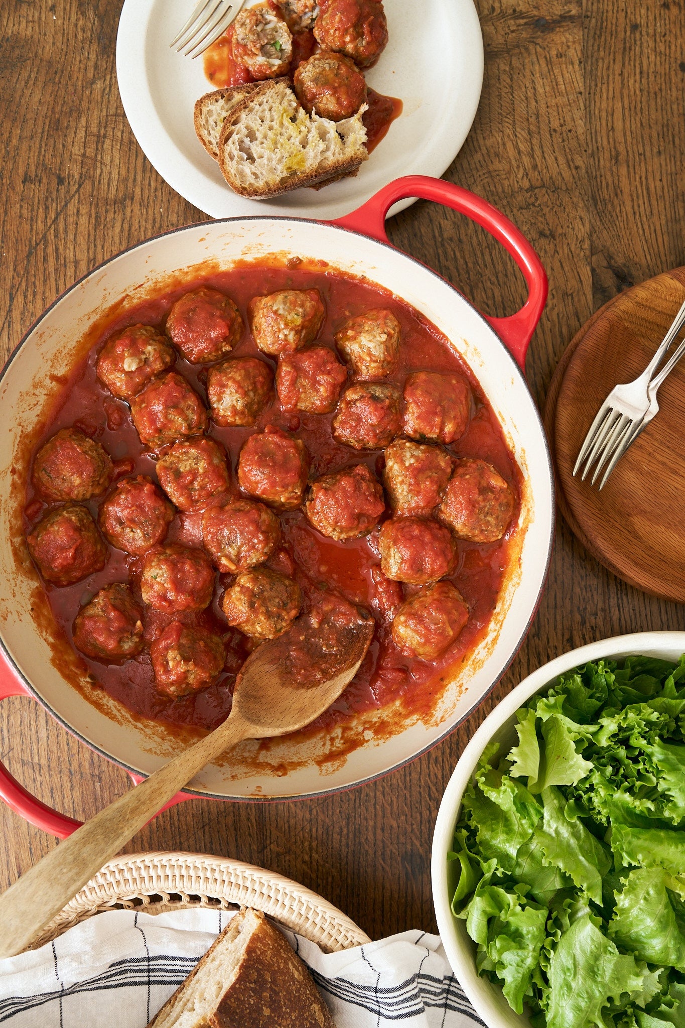 Dish of Italian Rice Meatballs in tomato sauce with a side of greens on a wooden table.